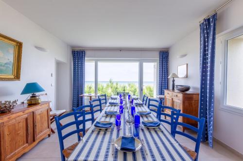 une longue table avec des chaises bleues dans une pièce avec une fenêtre dans l'établissement Villa de la Plage - à Ver sur Mer, à Ver-sur-Mer