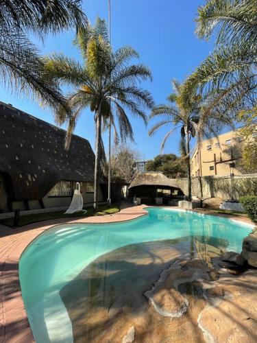 uma piscina com palmeiras e um edifício em The Eden Boulders Hotel and Resort Midrand em Midrand