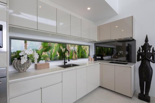 a white kitchen with white cabinets and a sink at Zog Villas in Koh Samui 