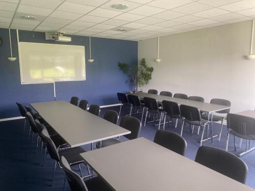 Danhostel Thorhallen Jels في Jels: قاعة اجتماعات مع طاولات وكراسي وشاشة عرض