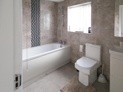 a bathroom with a tub and a toilet and a window at Pass the Keys Beautiful 3 bed home near MCR airport with parking in Cheadle