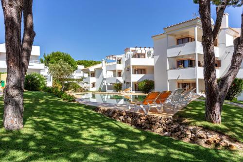 ein Gebäude mit Stühlen und Bäumen davor in der Unterkunft Fresh Sunny Flat with Pool & Terrace by Host Wise in Olhos de Água