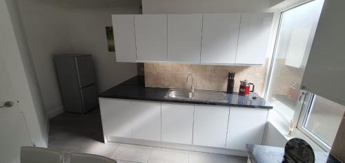 a kitchen with white cabinets and a sink at Lovely 3 Bedrooms Flat Near Romford Station With Free Parking in Romford