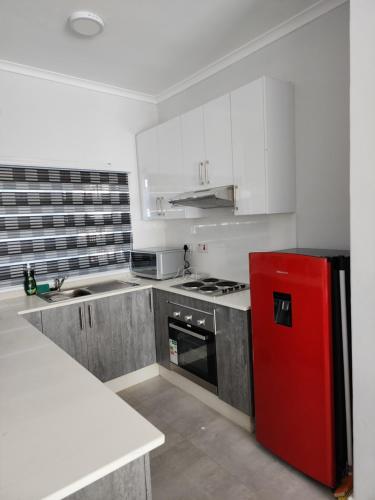 a kitchen with a red refrigerator and white cabinets at SaronaC102 in Gaborone