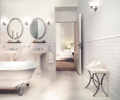 a white bathroom with a tub and two sinks and mirrors at Poseidonion Grand Hotel in Spetses