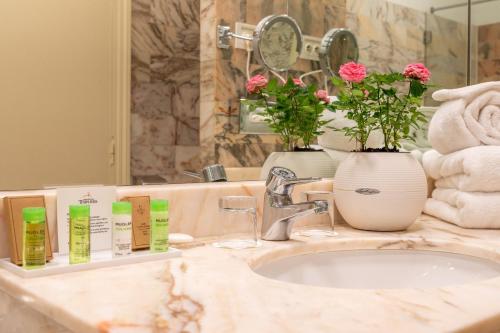 a bathroom counter with a sink and flowers on it at Grand Hôtel Des Templiers, Piscine & Spa in Reims