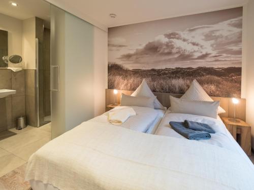 a bedroom with a large white bed with a painting on the wall at Inselsünn Hotel und Apartments in Spiekeroog