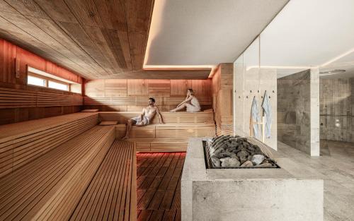 zwei Personen sitzen in einer Sauna mit Badewanne in der Unterkunft Falkensteiner Hotel & Spa Falkensteinerhof in Vals