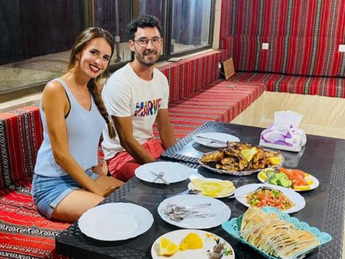 Um homem e uma mulher sentados à mesa com comida. em Wild Oryx Camp Bubbles em Wadi Rum