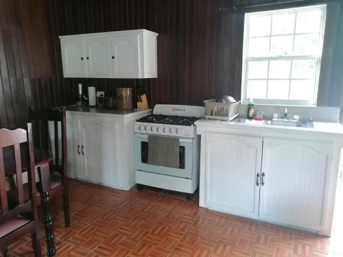 cocina con fogones, armarios blancos y fregadero en Belle Breeze Cottage en Gros Islet