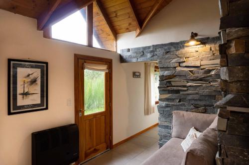 sala de estar con pared de piedra y ventana en Vuelvo al Sur Alojamiento Lago Puelo en Lago Puelo