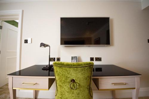 a desk with a green chair and a television on a wall at Best Western Abbots Barton Hotel in Canterbury