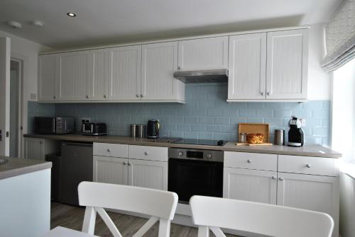 a white kitchen with white cabinets and white chairs at Murrays Neuk- stylish coastal apartment in Anstruther
