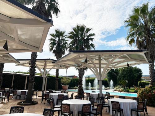 een patio met tafels, witte parasols en een zwembad bij Villa Sirena Hotel e Ricevimenti in Durazzano