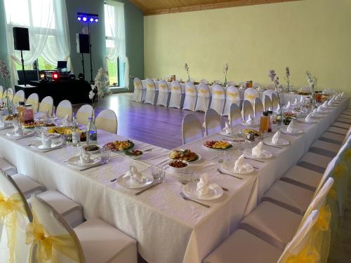 een lange tafel met witte stoelen en borden eten bij Auksi motell in Auksi