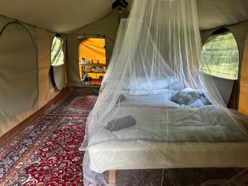 Bett in einem Zelt mit Moskitonetz in der Unterkunft Langø Feriecenter - Outdoor Lodge in Nakskov