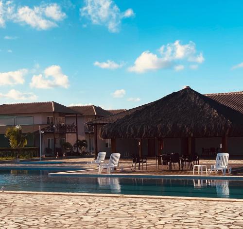 a pool with chairs and a table and a straw umbrella at Bangalô 39 in Tamandaré