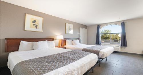 Budget Inn and Suites Stockton Yosemite في ستوكتون: غرفة فندقية بسريرين ونافذة