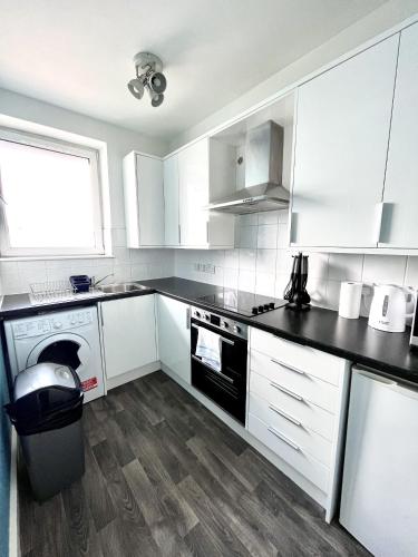 uma cozinha com armários brancos e um balcão preto em Modern 2 bed flat close to Shoreditch / Free Wi-Fi em Londres