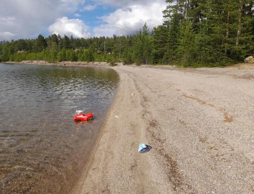 a beach with a red toy boat in the water at Empty Lots in Camping near Sandbach in Bräcke