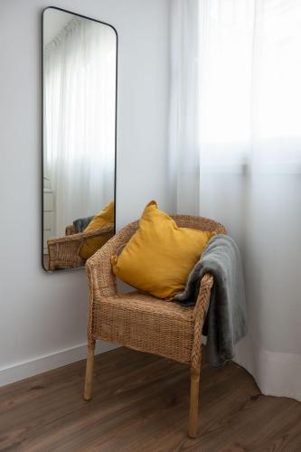 a wicker chair with a yellow pillow and a mirror at Apartamento Luis de Vargas in Huelva