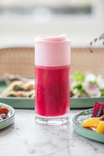 a red drink in a glass next to a plate of food at La Colombe d'Or Hotel in Houston