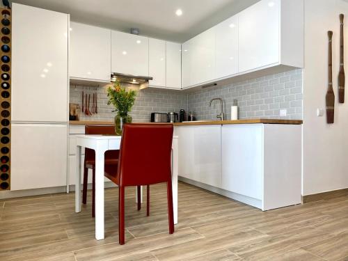 a kitchen with white cabinets and a table with red chairs at Casa Pirilampo Ferragudo in Ferragudo