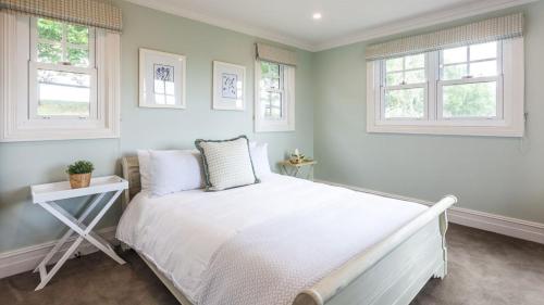 a bedroom with a white bed and two windows at Somerleyton Cottage in Wildes Meadow