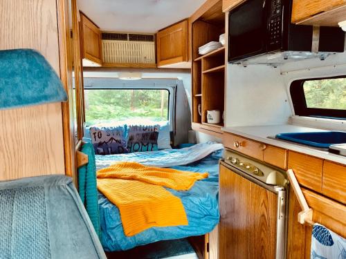 an rv with a kitchen and a bed in it at Shady Van in the Woods in Gillies Bay