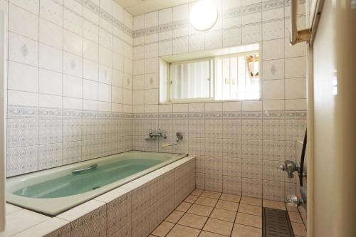 a bath tub in a tiled bathroom with a window at 民宿やまそ in Takashima