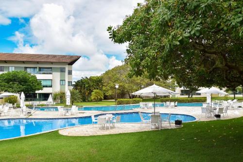 a pool with chairs and umbrellas next to a building at Carneiros Beach Resort - Flats Cond à Beira Mar in Praia dos Carneiros