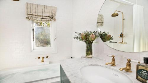 a white bathroom with a sink and a mirror at Werona Cottage - enchanting home in Burrawang