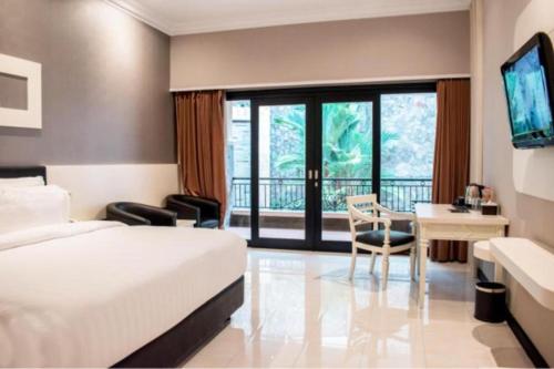 a hotel room with a bed and a desk and a television at Luminor Hotel Jember By WH in Jember
