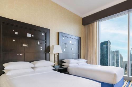 two beds in a hotel room with a large window at Marriott Marquis City Center Doha Hotel in Doha