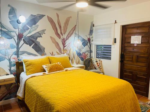 a bedroom with a yellow bed with a tropical wallpaper at Alux House in Placencia Village