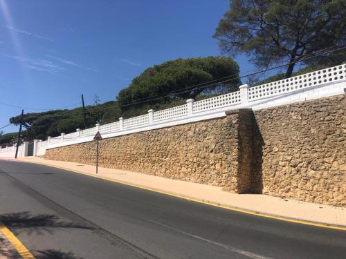 una pared de piedra con una valla blanca al lado de una carretera en Apartamentos Luxury Mazagón, en Palos de la Frontera