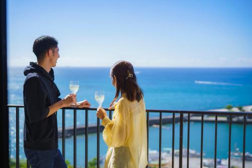 a man and a woman standing on a balcony with wine glasses at Moon Ocean Ginowan Hotel & Residence in Ginowan