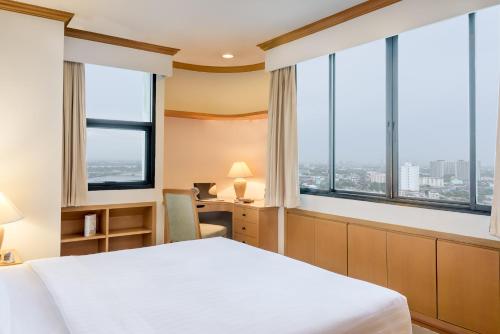 a bedroom with a bed and a desk with windows at Riverine Place Hotel and Residence in Nonthaburi