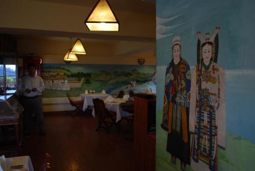 a woman standing in a restaurant with a painting on the wall at Chonor House in McLeod Ganj