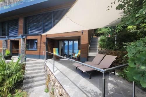 ein Haus mit einer Terrasse mit einem Stuhl und einem Sonnenschirm in der Unterkunft Villa Bootsmann mit spektakulärer Seesicht und Badeplatz in Vitznau