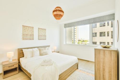 a white bedroom with a bed and a window at Voyage One Bedroom In Mayan in Abu Dhabi