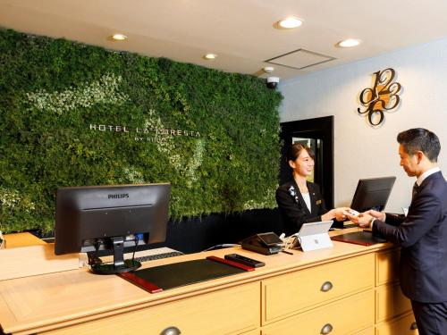 two people standing at a desk with a computer at Hotel La Foresta By Rigna in Fukuoka