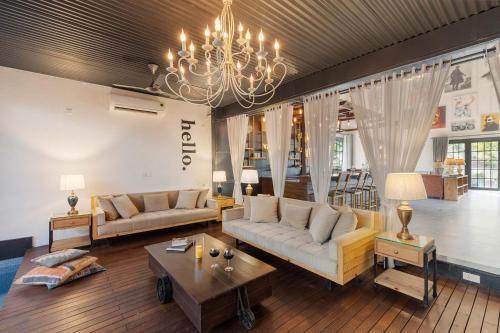 a living room with two couches and a chandelier at StayVista's The Barn House - Farm-View Villa with with bonfire, Indoor Pool & Bar in Chandīgarh