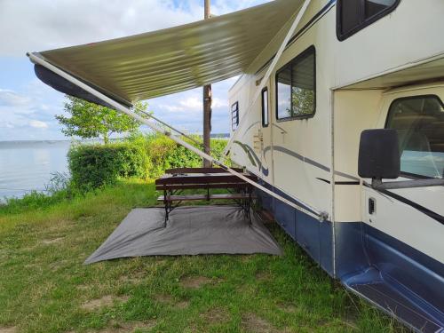 an rv with a picnic table in front of the water at KAMPER NAD BRZEGIEM JEZIORA NIEGOCIN in Giżycko