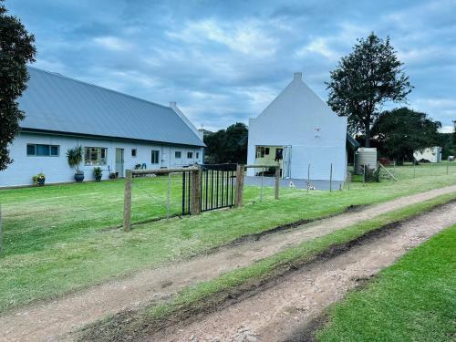 a white barn with a fence next to a dirt road at Doornboom Farm Self Service in Heidelberg