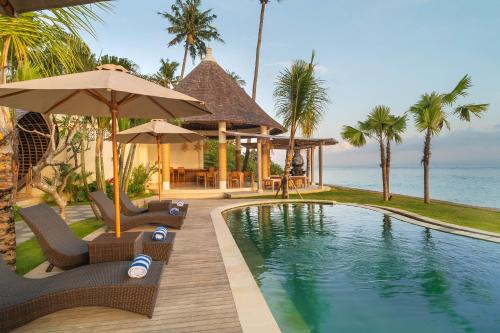 un complejo con una piscina con sillas y sombrillas en The Sankara Beach Resort - Nusa Penida en Nusa Penida