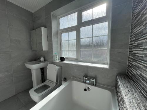 La salle de bains est pourvue d'une baignoire, de toilettes et d'une fenêtre. dans l'établissement Luxurious Kitchen Lrg Bedrooms Holiday FreeParking, à Luton