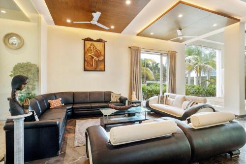 Elle comprend un salon doté d'un mobilier en cuir et d'une grande fenêtre. dans l'établissement Timeless Elegance by StayVista - Poolside Villa with Lawn & Terrace, à Kolkata