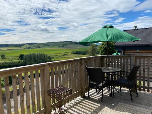 a table and chairs on a deck with a green umbrella at Badger Lodge with Hot Tub in Cupar