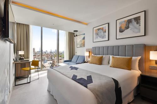 ロンドンにあるRiu Plaza London Victoriaの大きなベッドとデスクが備わるホテルルームです。